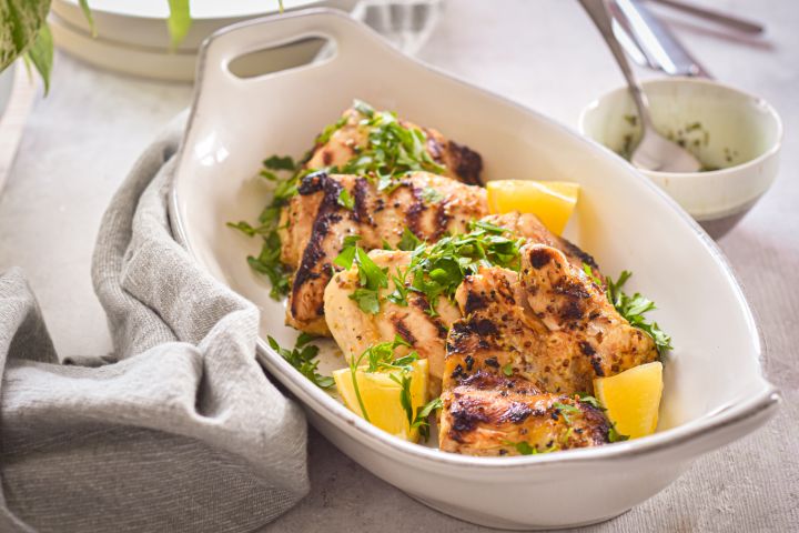 Grilled Lemon Dijon Chicken Thighs Grilled lemon dijon chicken thighs with fresh lemon and parsley in a white dish with a linen napkin.