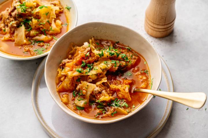Healthy Cabbage Soup A bowl of hearty cabbage soup with ground meat, garnished with fresh parsley, sits on a light gray surface. A second bowl and pepper mill in the background.