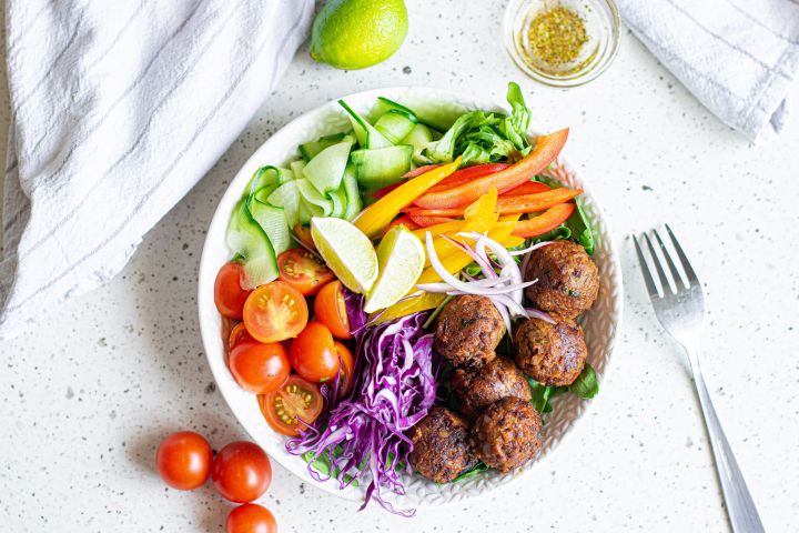 Lentil Meatballs (Quick and Easy) Lentil meatballs served in a bowl with cabbage, peppers, tomatoes, cucumber, red onion, and limes.