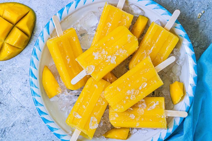 Mango Popsicles Mango popiscles made with fresh mango pieces, lime juice, water, and honey on a plate with ice.