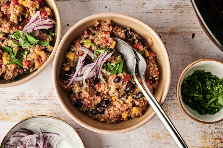 Mexican Quinoa (Slow Cooker, Instant Pot, or Stovetop) Bowls of cooked Mexican quinoa topped with fresh red onion slices and chopped cilantro, ready to be served with additional toppings on the side.