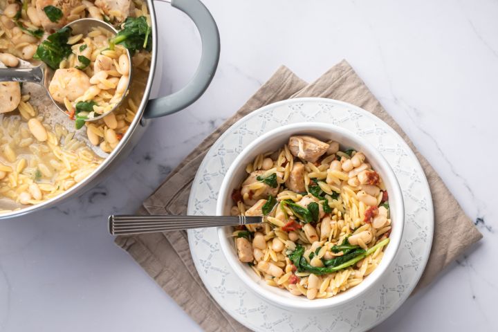 One Pot Orzo Pasta with Chicken Orzo pasta with chicken breast, spinach, tomatoes, and white beans served in a bowl with Parmesan cheese.