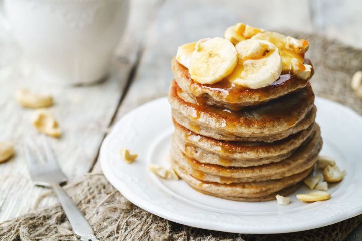 Protein Packed Oatmeal Banana Pancakes Banana oatmeal pancakes served in a stack with sliced bananas and maple syrup.