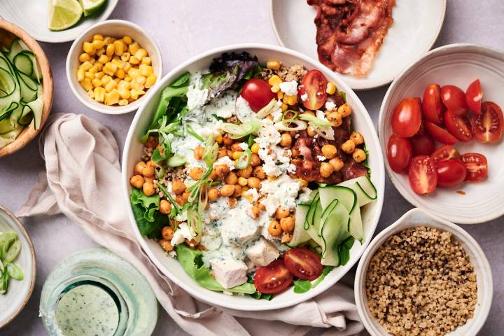 Protein Packed Salad Bowls Protein packed salad bowls with chicken, bacon, chickpeas, cucumbers, quinoa, cherry tomatoes, green onions, and cottage cheese dressing.
