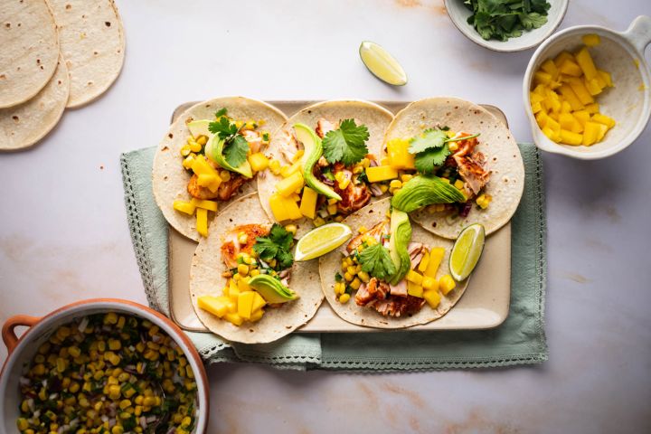Salmon Tacos with Corn Salsa Salmon tacos with corn salsa, mango, fresh avocado slices, and lime wedges on a tray.