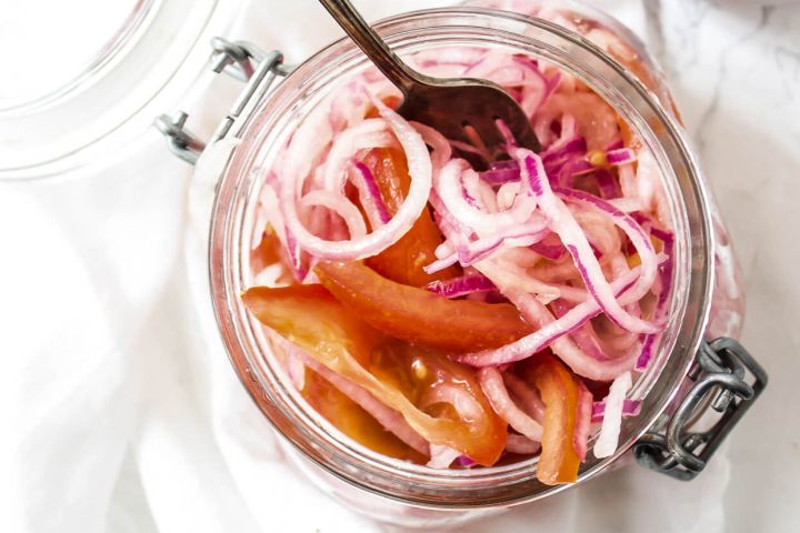 Peruvian Salsa Criolla Salsa criolla with red onions, tomatoes, and lime juice in a glass jar with a spoon.