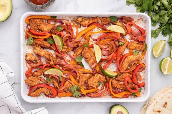 Sheet Pan Chicken Fajitas (5 Ingredients!) Sheet pan chicken fajitas with chicken breast, peppers, onions, and limes on a baking sheet .