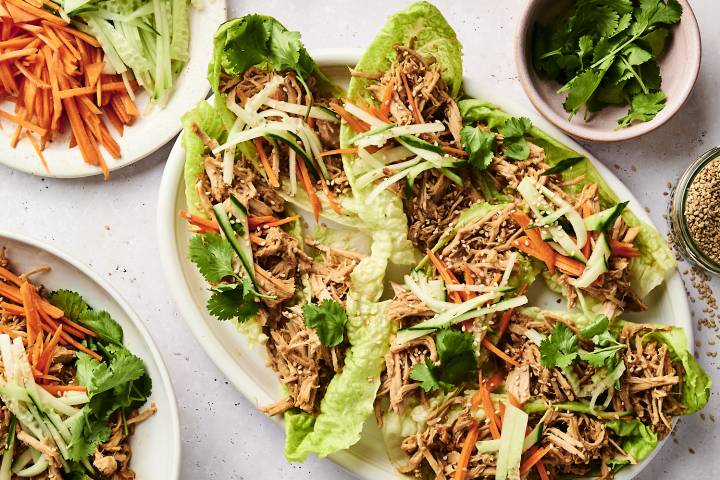 Slow Cooker Banh Mi Pork A platter of lettuce wraps filled with shredded chicken, carrot and cucumber julienne, topped with sesame seeds and fresh cilantro.