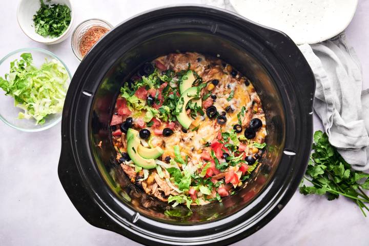 Slow Cooker Chicken Enchilada Casserole Slow cooker chicken enchilada casserole in a crockpot with avocado, black olives, lettuce, and tomatoes.