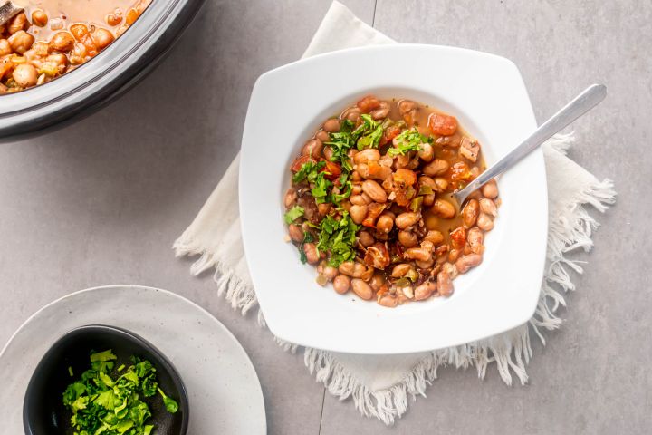 Slow Cooker Charro Beans (Frijoles Charros) Slow cooker frijoles charros, cowboy beans, in a bowl with creamy pinto beans, jalapenoes, tomatoes, onions, and fresh cilantro.