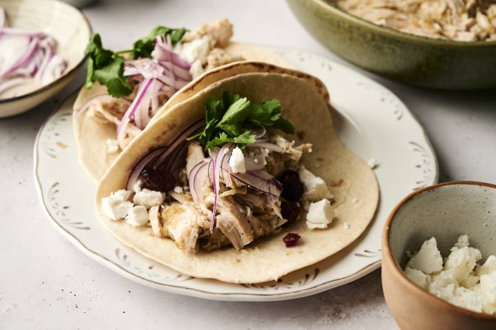 Slow Cooker Turkey Tacos Shredded turkey tacos with red onion, cilantro, dried cranberries, and crumbled cheese on soft flour tortillas.