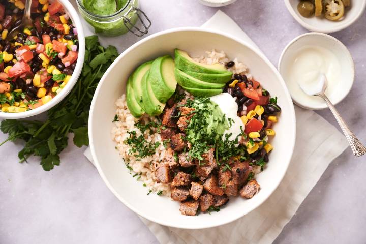 Southwest Steak Bowls Southwest steak bowls with cooked steak, rice, black beans, cilantro, corn, pico de gallo, avocado, and sour cream.