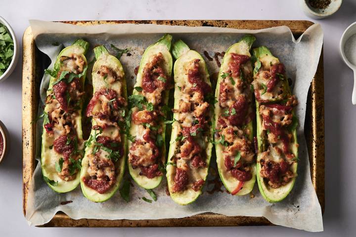 Zucchini Taco Boats Baked Tex-Mex stuffed zucchini with cheese, tomato sauce, and cilantro on a parchment-lined baking tray.