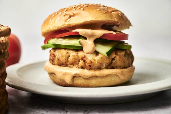 Tilapia Fish Burgers Tilapia fish burger with sauce cucumber and tomato on a sesame seed bun.