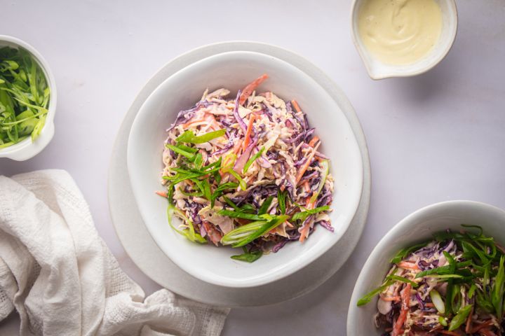 Tricolor Coleslaw Tricolor coleslaw with red cabbage, green cabbage, and carrots in a bowl with yogurt dressing and green onions.