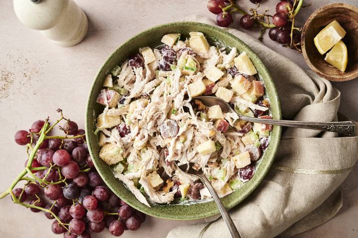 Waldorf Chicken Salad Overhead view of Waldorf chicken salad in a green bowl, made with shredded chicken, red grapes, celery, apples, and walnuts, served with two spoons.