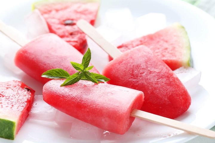 Healthy Watermelon Popsicles Two watermelon popsicles with a block of ice.