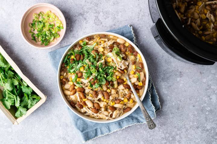Easy White Chicken Chili A hearty bowl of chicken chili topped with fresh cilantro and sliced green onions. A dish of green onions and fresh cilantro beside it, exuding a cozy feel.