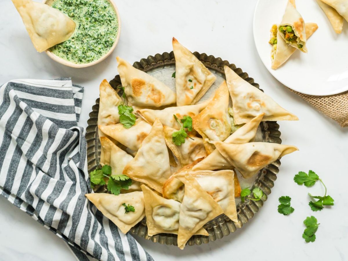 Vegetarian Lunches Baked samosa filled with potato, cauliflower, and peas on a plate with cilantro and mint dipping sauce.
