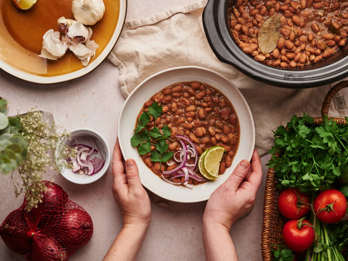 Mexican Side Dishes Crockpot pinto beans in a bowl with red onions, cilantro, lime slices, and other vegetables.