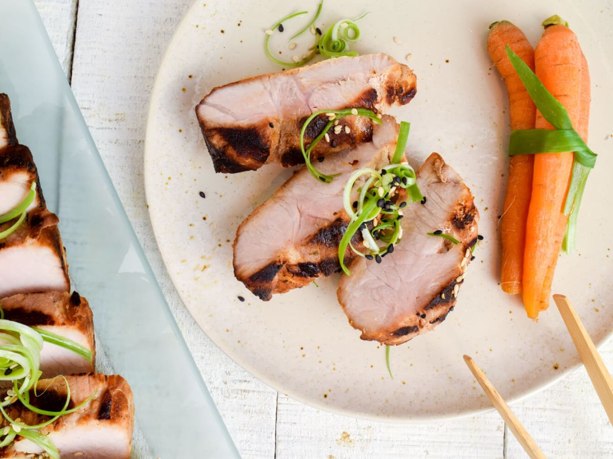 Quick and Easy Pork Dinner Recipes Asian grilled pork tenderloin on a plate with carrots, green onions, and chopsticks.