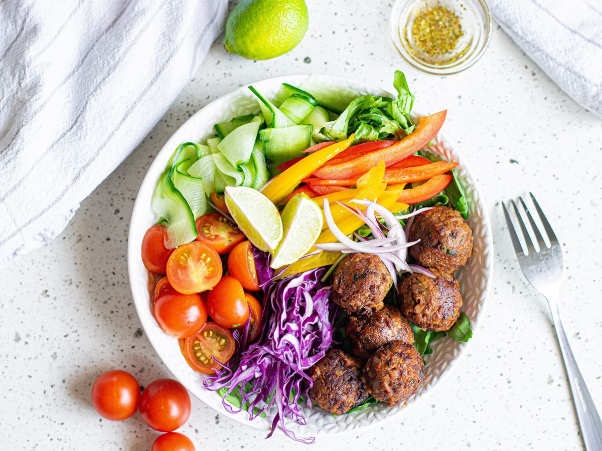 Quick and Easy Vegetarian Dinner Recipes Lentil meatballs served in a bowl with cabbage, peppers, tomatoes, cucumber, red onion, and limes.
