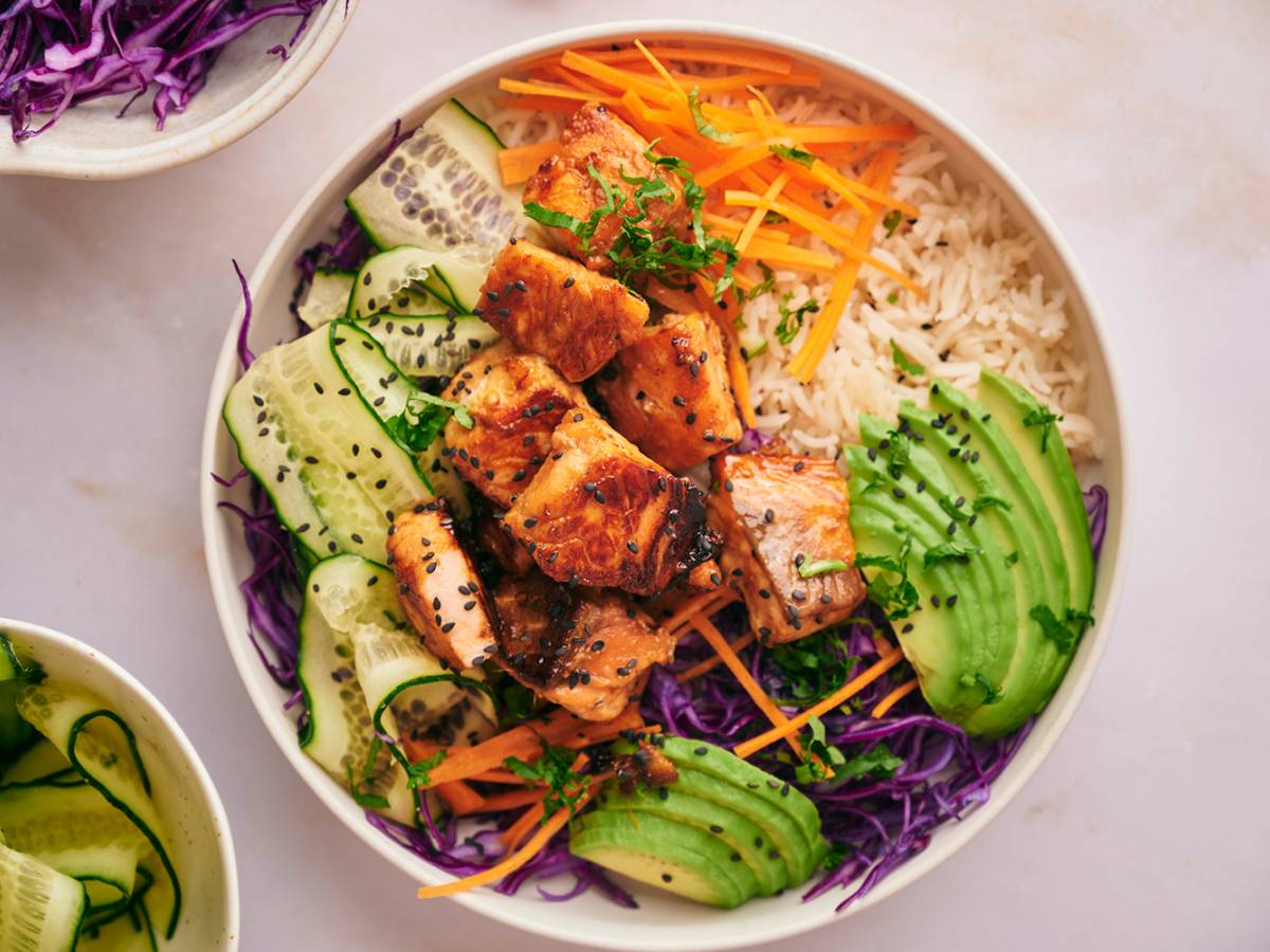 Healthy Bowl Recipes Salmon rice bowl with salmon pieces that are crispy served with rice, purple cabbage, edamame, carrots, and cucumber.