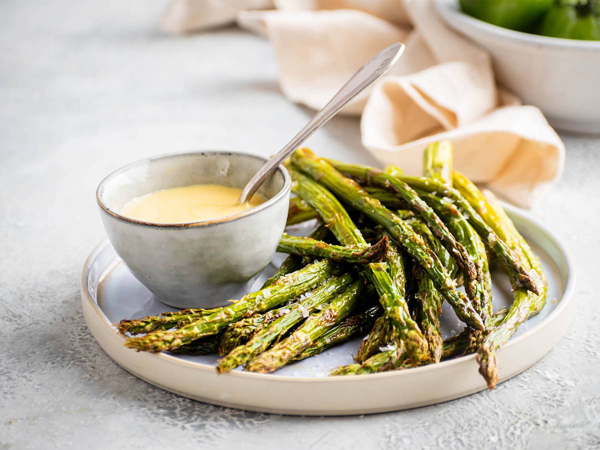Healthy Eating Roasted asparagus with olive oil, salt, and pepper served on a plate with hollandaise sauce.