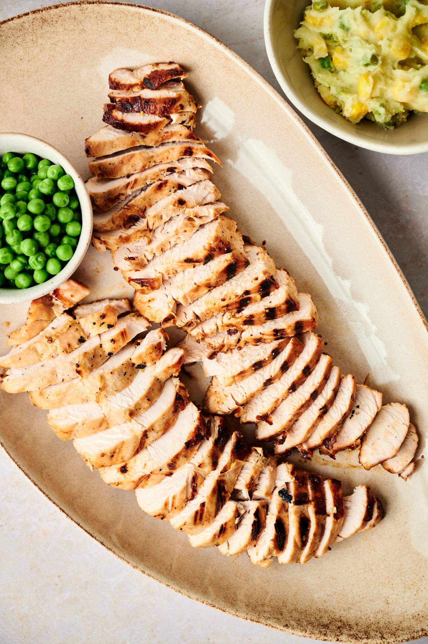 Turkey breast tenderloin that has been grilled and sliced on a platter with peas.
