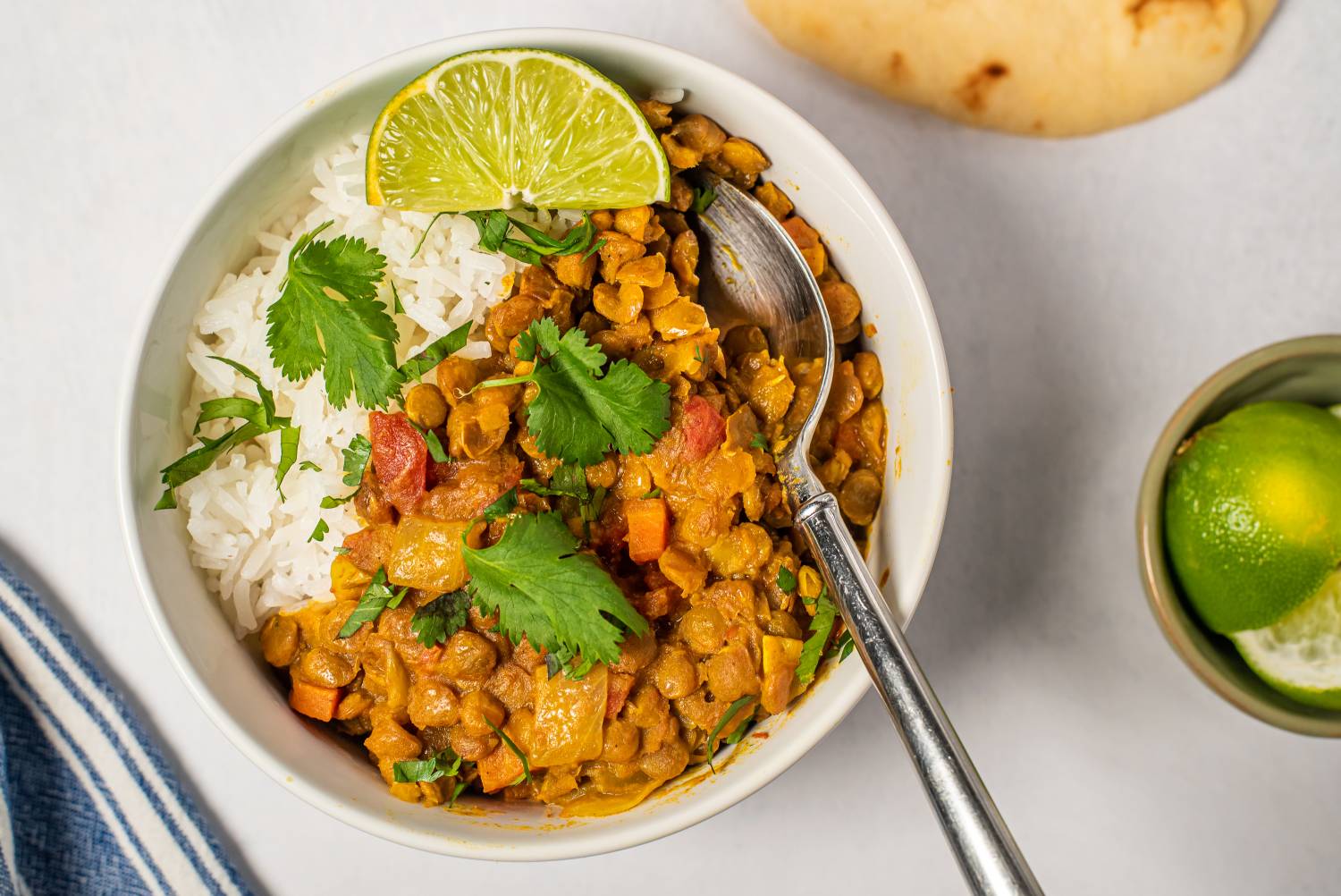 Bowls of lentil coconut curry served over white rice, garnished with fresh cilantro and lime wedges.