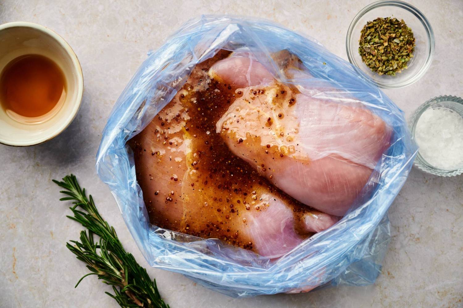 Turkey breast tenderloins marinating in a ziploc bag with rosemary on the side.