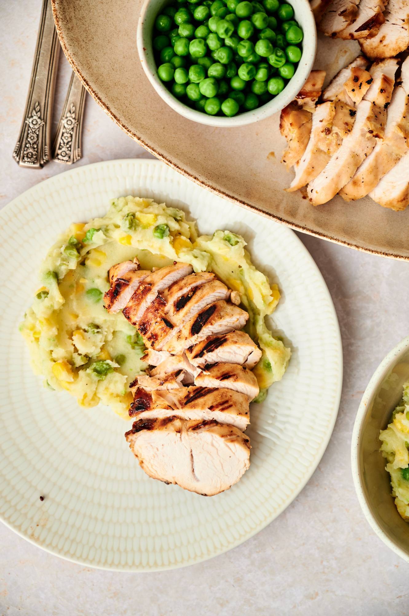 Sliced grilled turkey breast on a bed of mashed potatoes with peas and carrots.