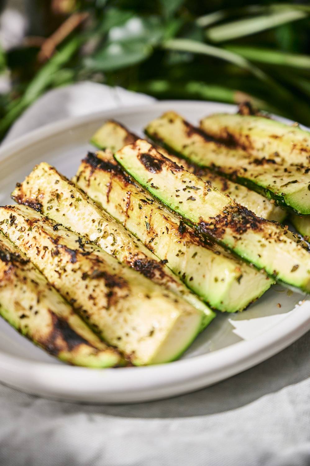 Grilled spears of zucchini on a plate with fresh herbs and spices.