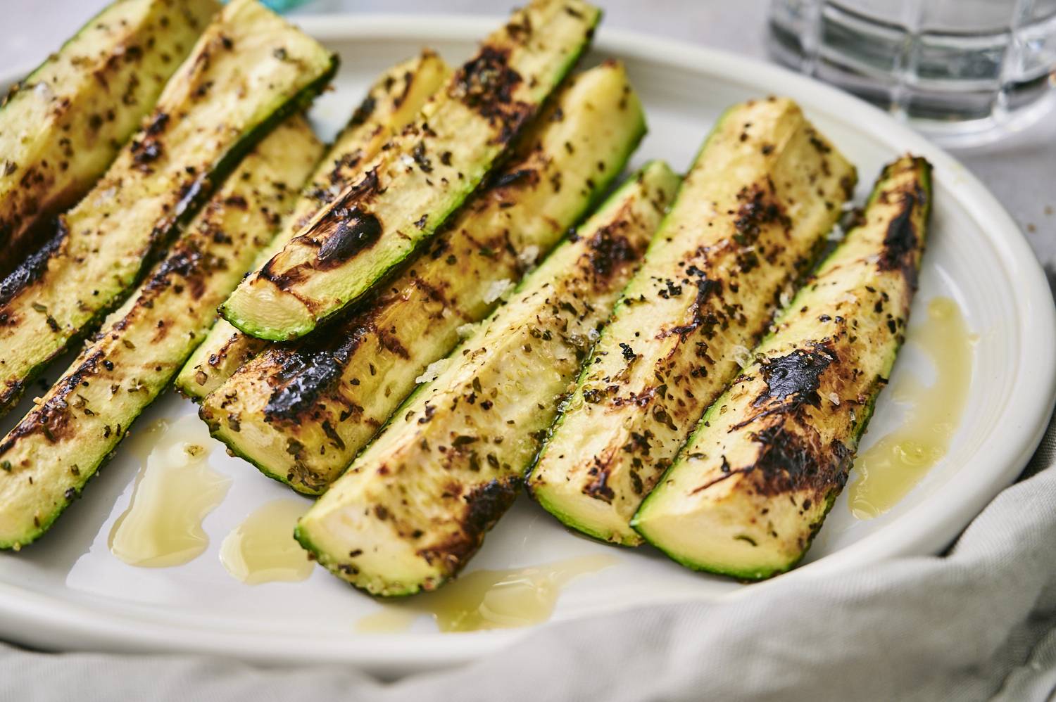 Tender grilled zucchini with charred grill marks served on a plate with dried herbs and garlic.
