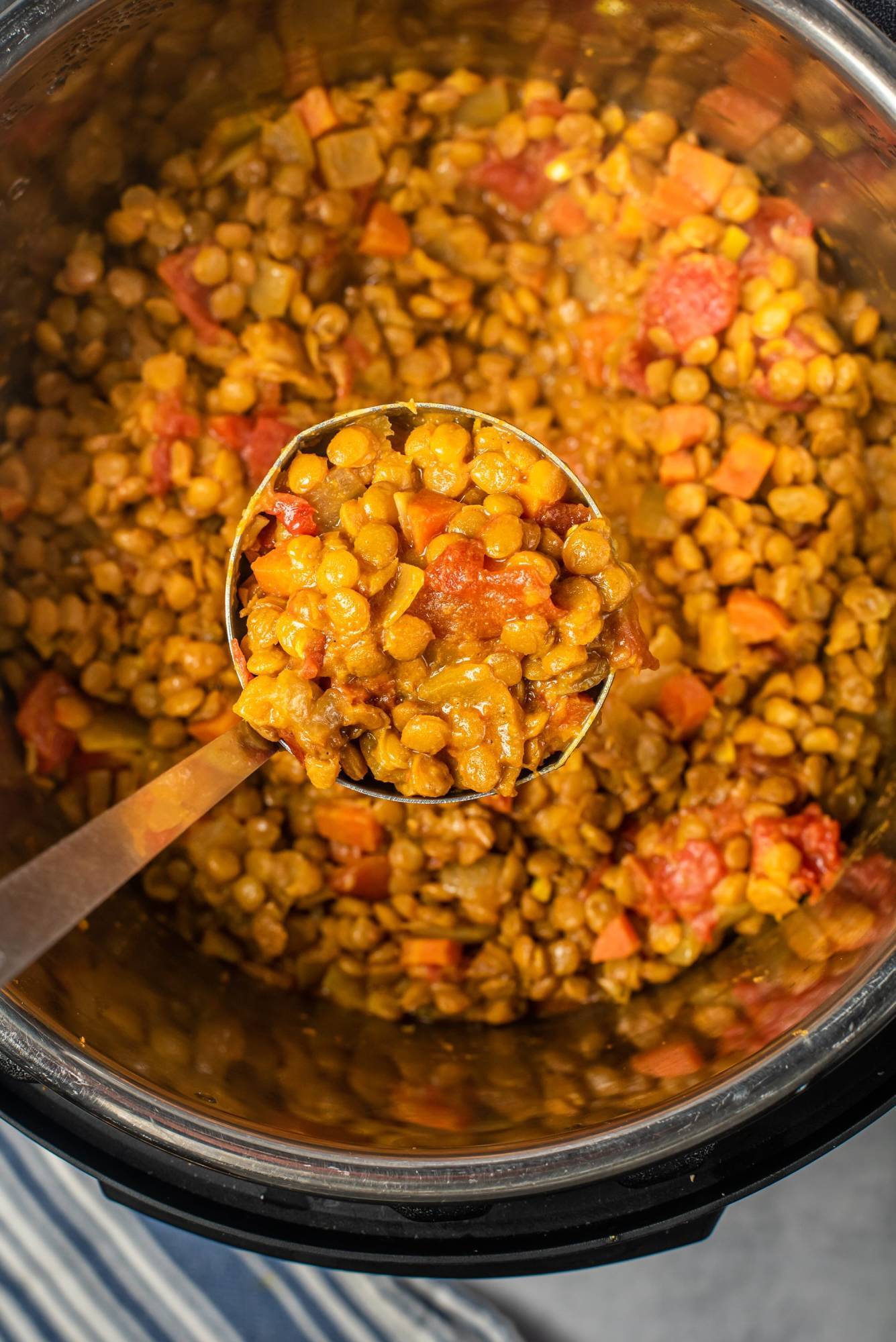 A ladle scooping up hearty lentil coconut curry from an Instant Pot, filled with tender lentils, tomatoes, and vegetables.