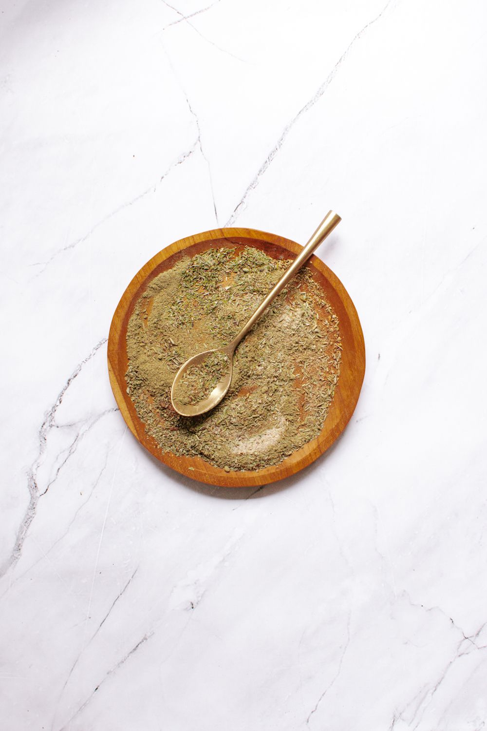 Homemade chicken seasoning with thyme, rosemary, sage, and other herbs on a wooden plate.