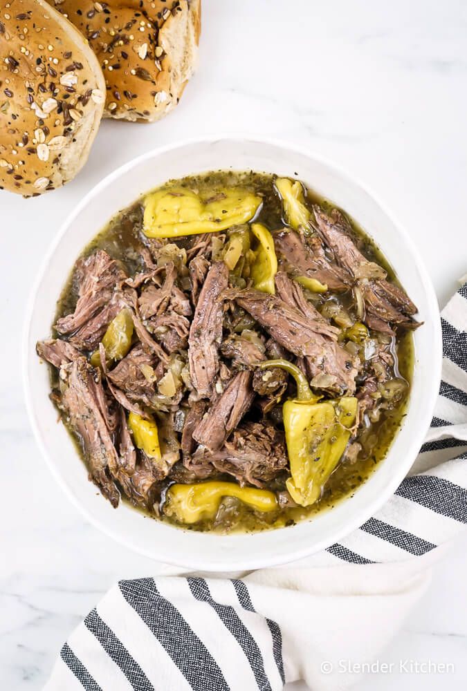 Pepperoncini Italian beef in a bowl with pepperoncinis and onions with rolls on the side.