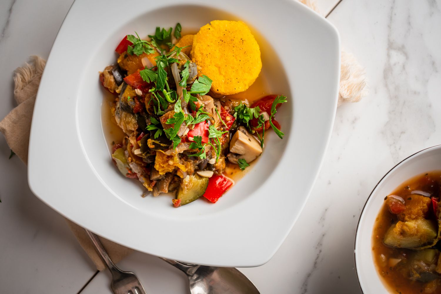 Ratatouille with zucchini, eggplant, tomatoes, onions, and summer squash in a bowl with fresh herbs and polenta rounds.