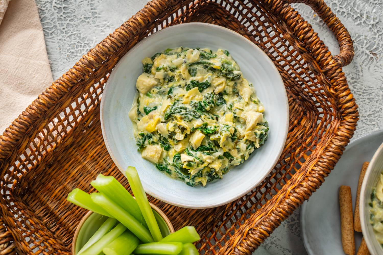 A bowl of creamy spinach, artichoke, and kale dip in a woven basket.