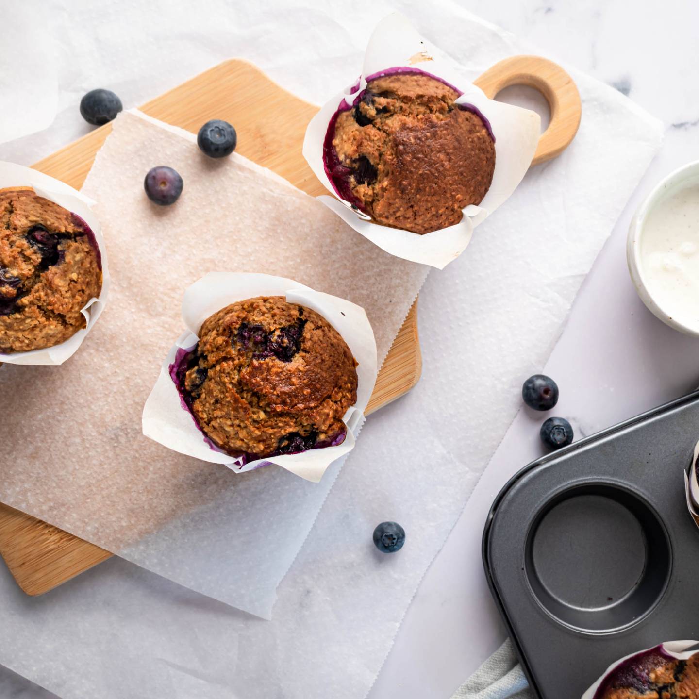 Blueberry oatmeal muffins with fresh blueberries in parchment paper on a cutting board.