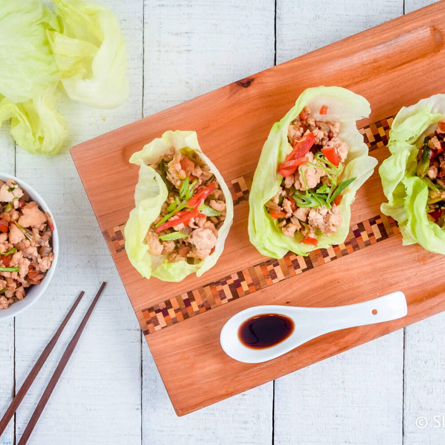 Chicken lettuce wraps on a wooden board with ground chicken and veggies in a hoisin sauce.