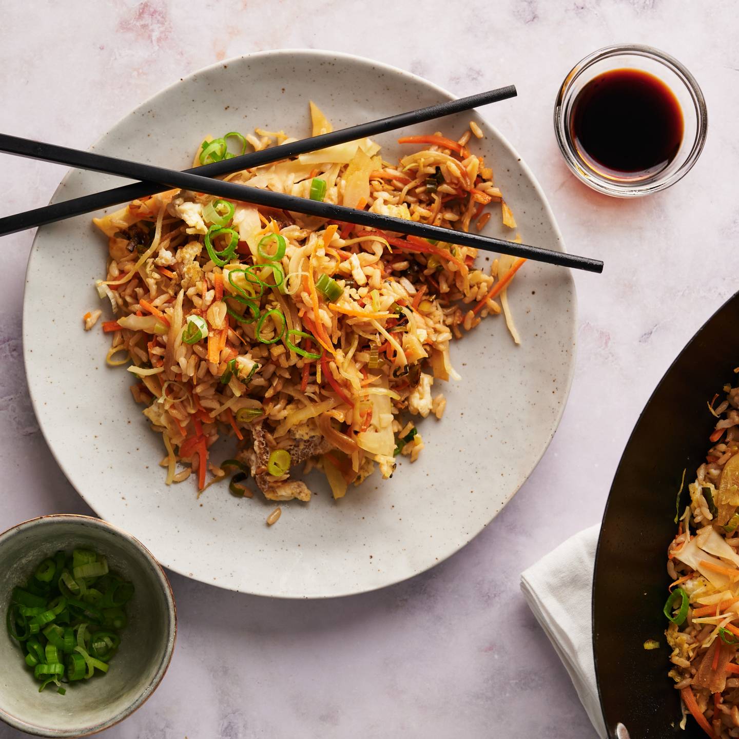 Healthy fried rice with cabbage, carrots, and vegetables served on a plate with chopsticks and in a wok.