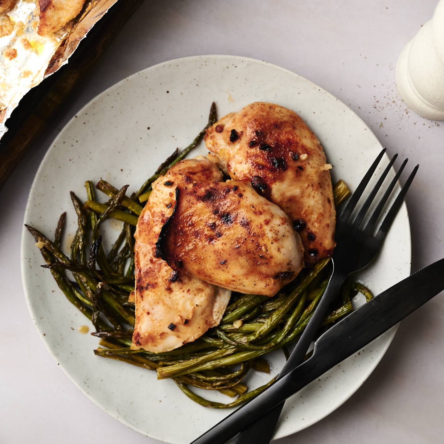 A plate of cooked honey garlic chicken and asparagus, garnished with sesame seeds and fresh parsley.