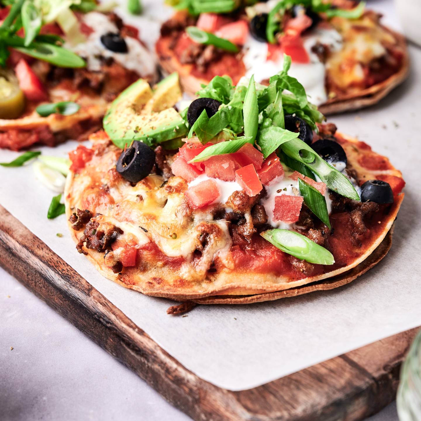 Mexicna pizzas with ground beef, refried beans, crispy corn tortillas, and melted cheese topped with lettuce, tomatoes, jalapenos, and sour cream.