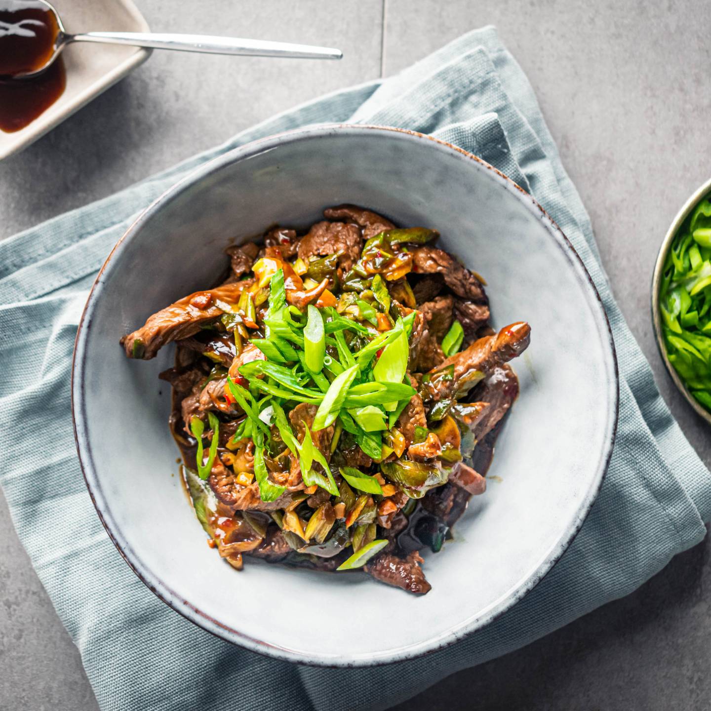 Healthy Mongolian Beef in a bowl with chopsticks with scallions and sesame seeds.