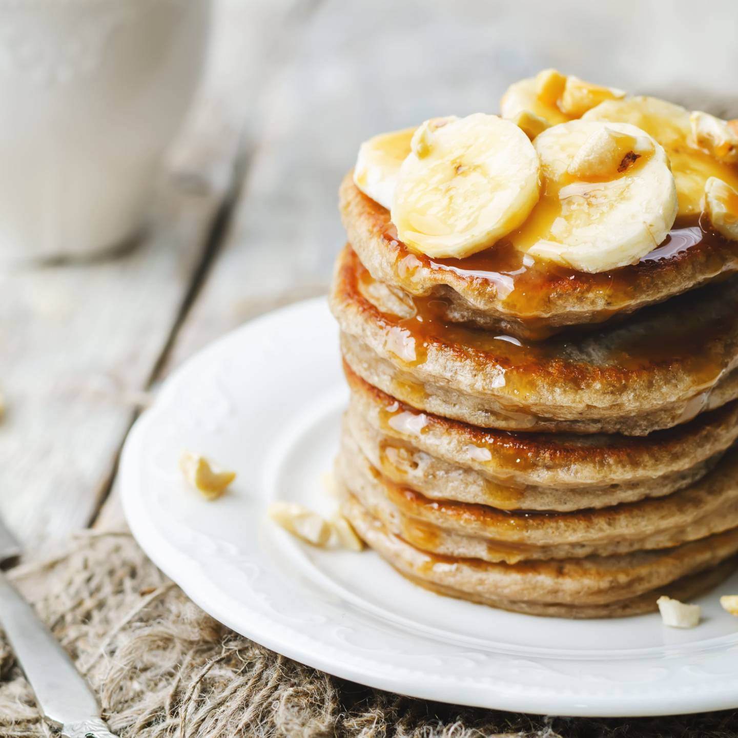Banana oatmeal pancakes served in a stack with sliced bananas and maple syrup.