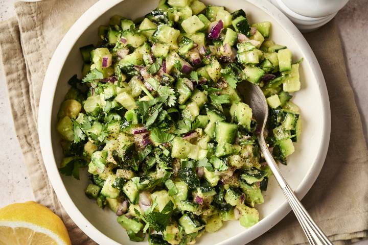 Close-up of avocado cucumber salsa in a white bowl, garnished with fresh cilantro and black pepper, with a spoon ready for serving.
