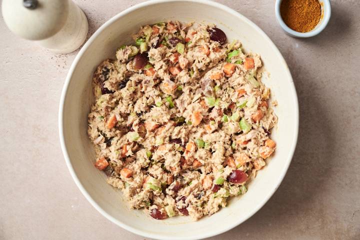 Curry tuna salad with grapes, carrots, and celery in a white bowl, with curry powder in a small dish on the side.