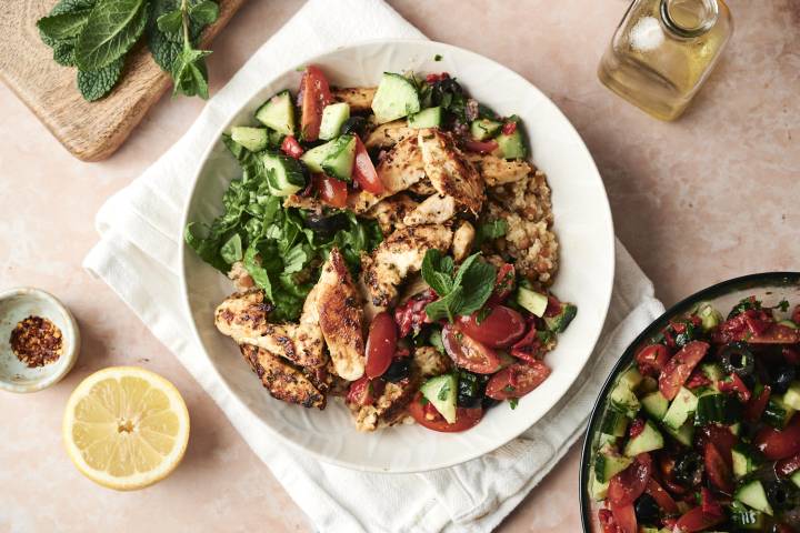 A dish featuring grilled chicken, fresh vegetable salad, lettuce, and grains, topped with fresh mint leaves.