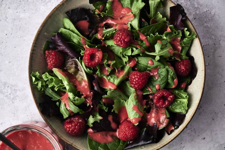 Fresh mixed greens topped with ripe raspberries and drizzled with a vibrant raspberry dressing in a decorative bowl.